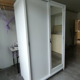 ตู้เสื้อผ้าบานเลื่อนเหล็กสีขาว กระจกเงาด้านข้าง วางอยู่ในห้องมีประตูหน้าห้องเปิดอยู่